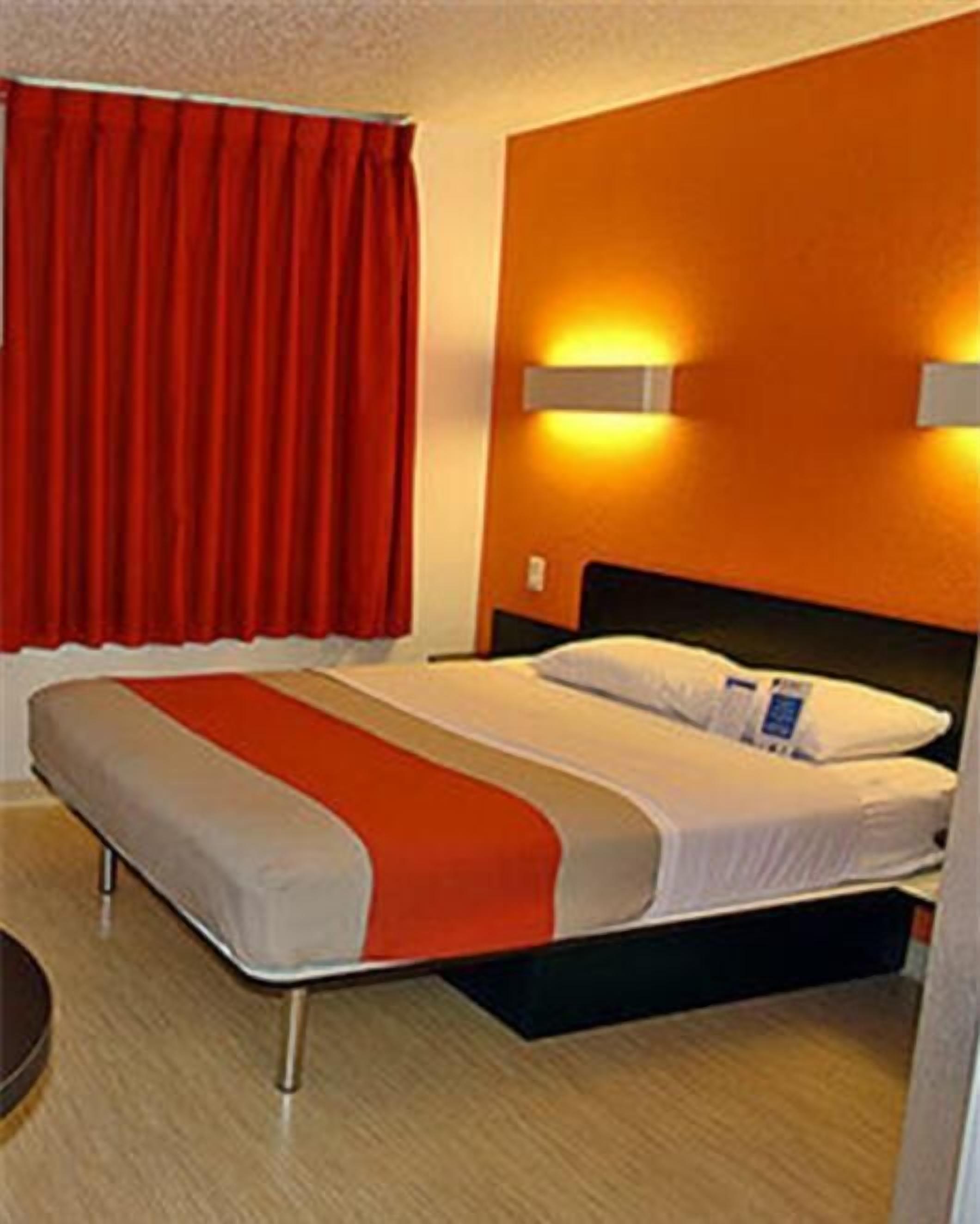 A hotel room with a bed, red curtains, and wall-mounted lights.