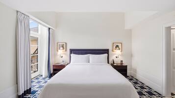 A hotel room with a bed, two bedside tables with lamps, a window with curtains, and a patterned floor.