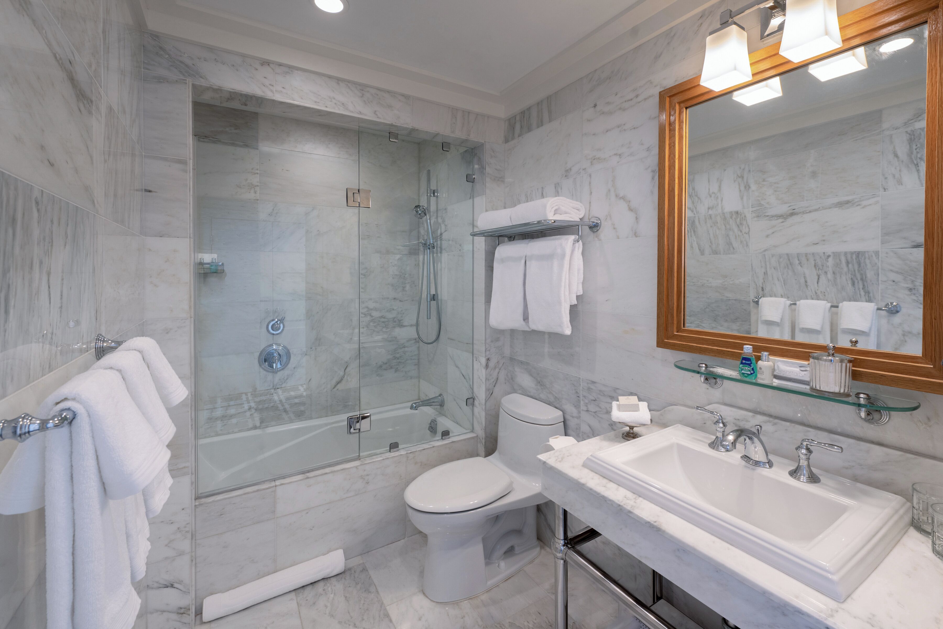 A modern bathroom with a glass-enclosed shower, a white toilet, and a large sink with a mirror above.