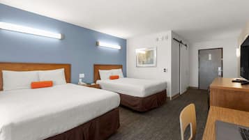 Quarto de hotel com duas camas, uma mesa com um laptop, uma cadeira, uma porta e um aplique na parede.