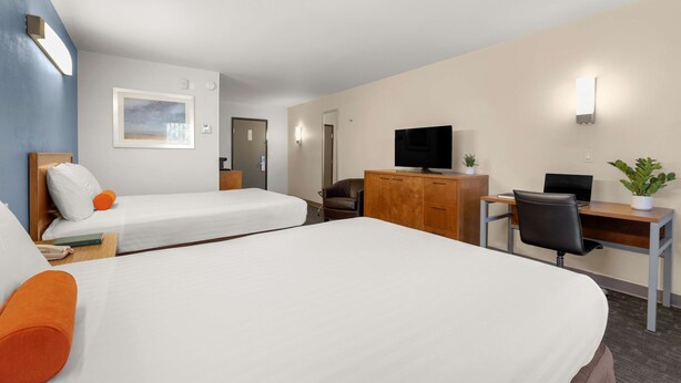 A hotel room with two beds, a desk with a computer, a television, and a small plant. - Good Nite Inn - Redwood City (Redwood City)