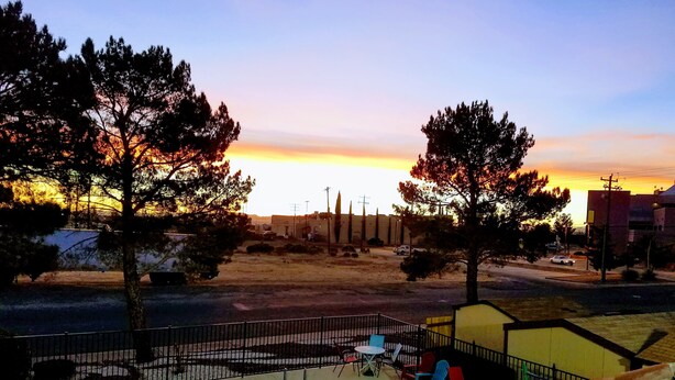 A swimming pool with a fenced area, outdoor seating, and a view of a sunset over a landscape with trees and buildings. - Rodeway Inn near Ft Huachuca (Sierra Vista)