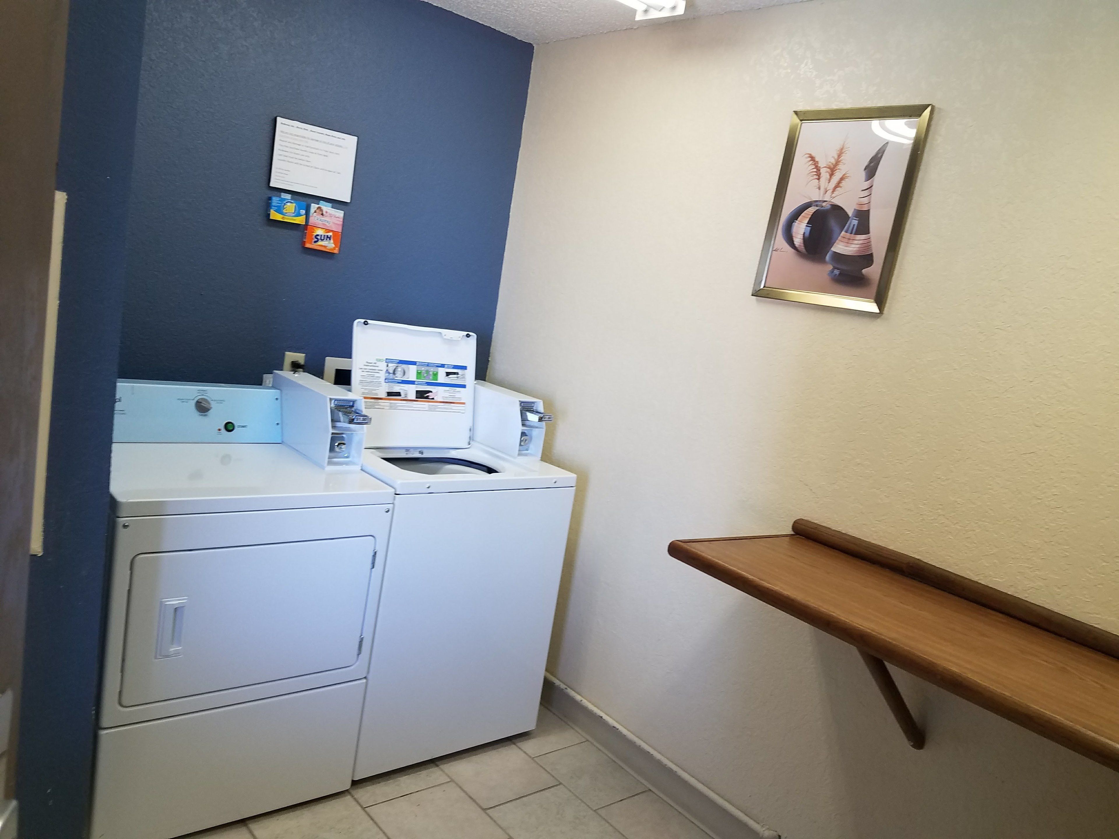 A laundry area with stacked washers and dryers, a bulletin board, and a wooden bench.