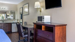 A hotel room with a bed, a desk with a lamp, a microwave, a TV, a mirror, and a small kitchenette. - Rodeway Inn near Ft Huachuca (Sierra Vista)