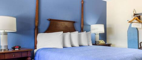 A hotel room with a large bed, two bedside tables, a nightstand, a hanging laundry rack, and a wall clock.