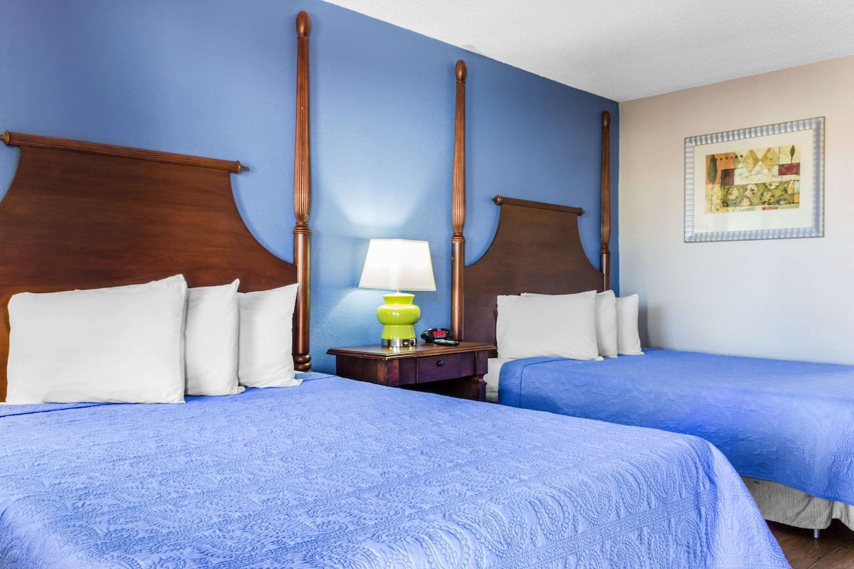 A hotel room with two beds, a nightstand with a lamp, and a framed artwork on the wall.
