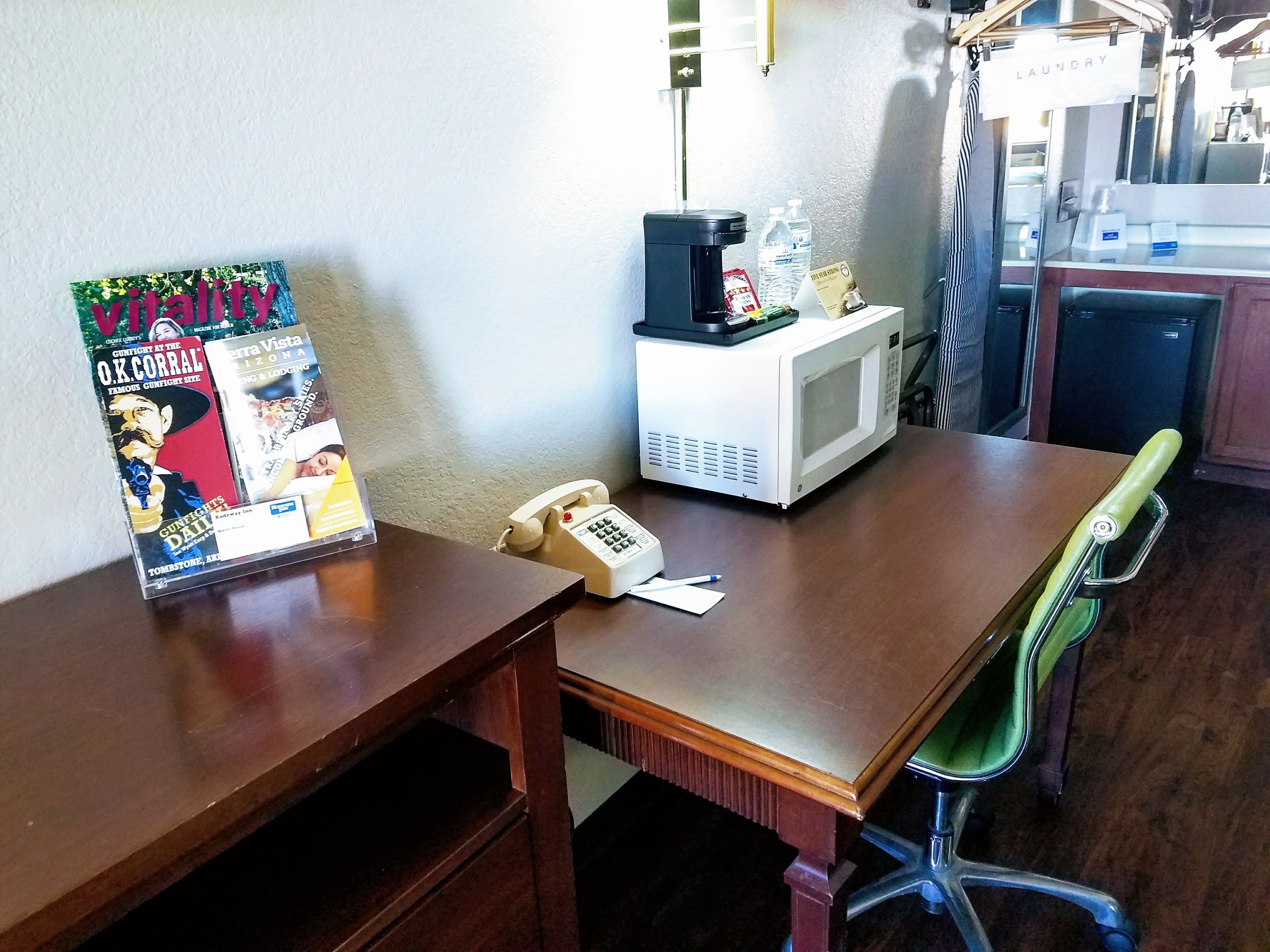 A small office with a wooden desk, a telephone, a microwave, and a bulletin board with magazines.