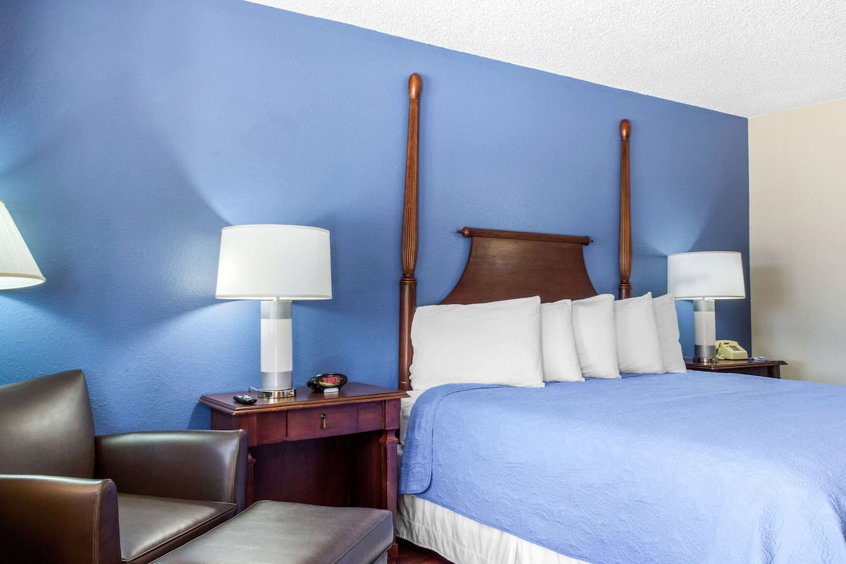 A hotel room with a large bed, two bedside tables, a chair, and a lamp.