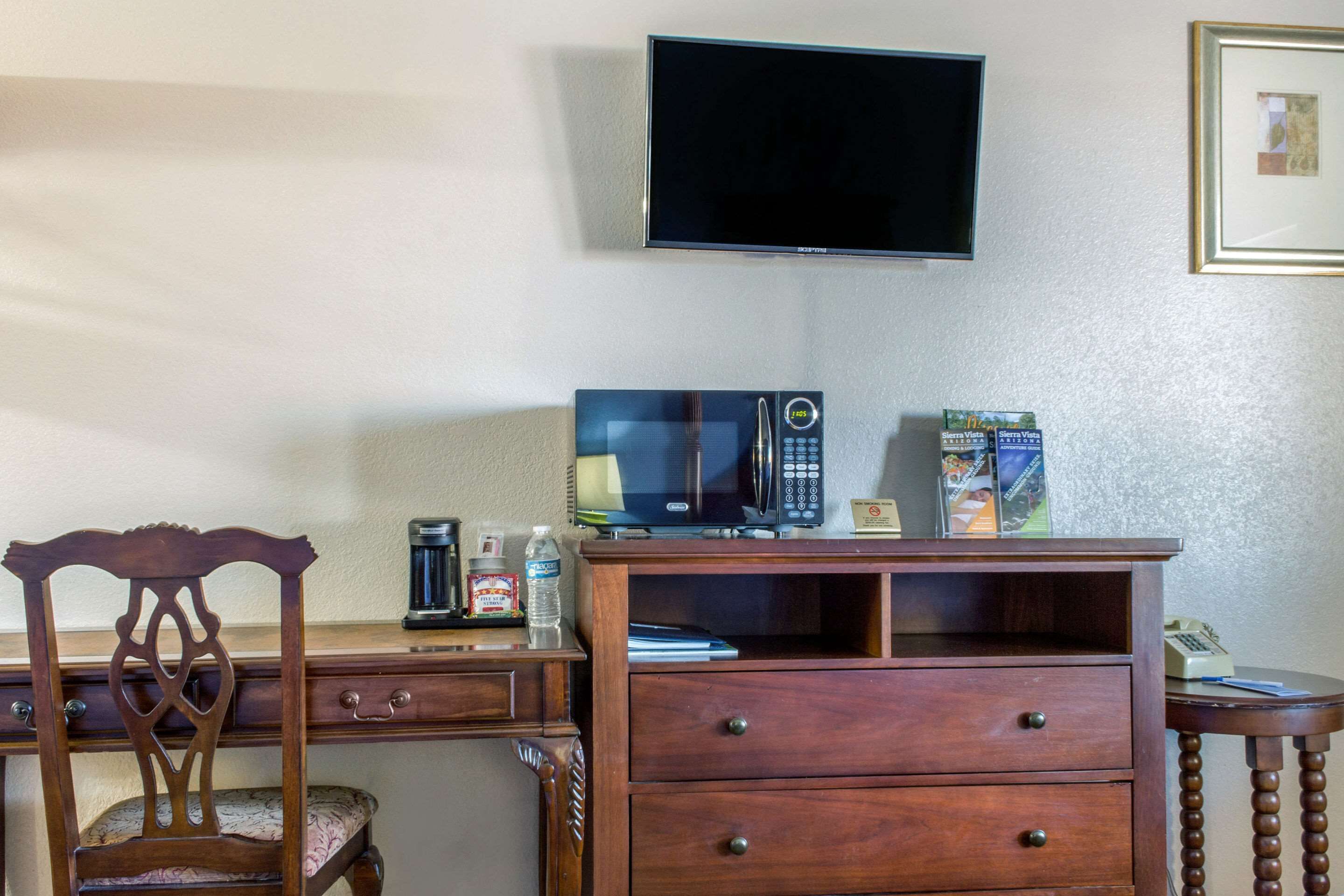 A wooden desk with a television mounted on the wall, a chair, and a small table with a telephone.