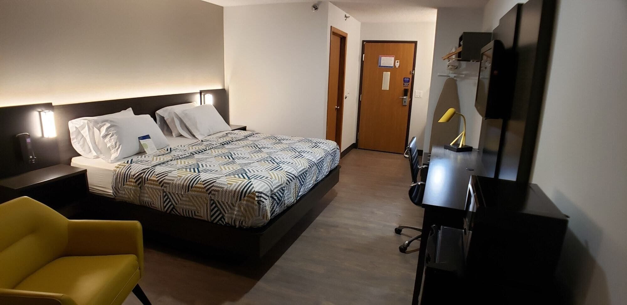 A hotel room with a bed, a desk, a chair, a TV, and a door.