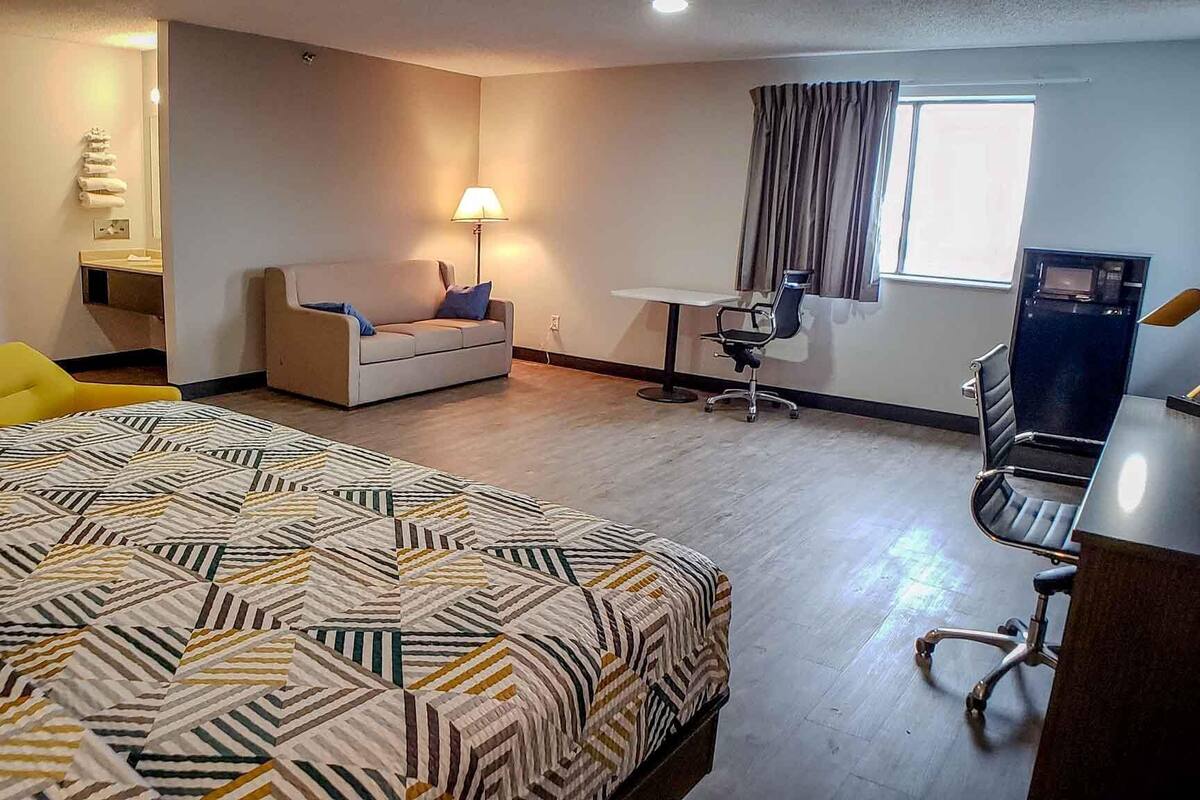 A hotel room with a large bed, a sofa, a desk, a chair, and a window with curtains.