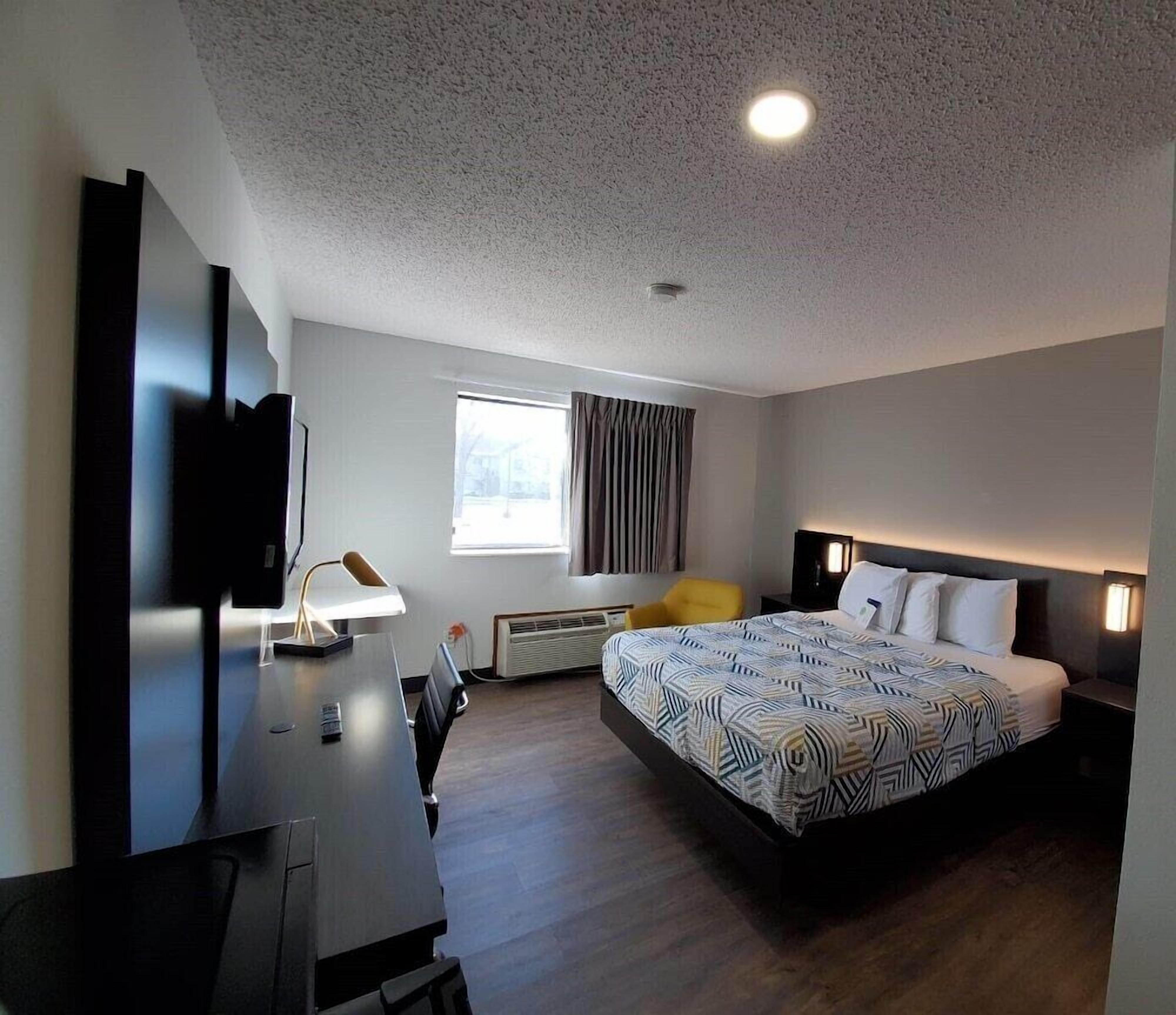 A modern hotel room with a large bed, a desk with a chair, a flat-screen TV, and a window with curtains.