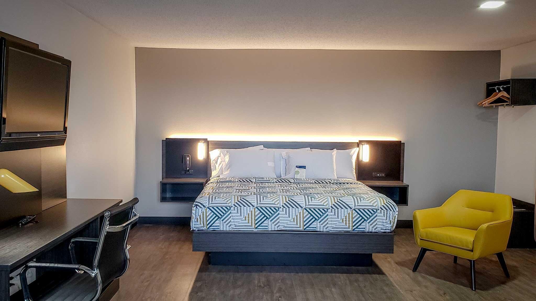 A hotel room with a bed, bedside tables, a desk, a chair, and a TV.