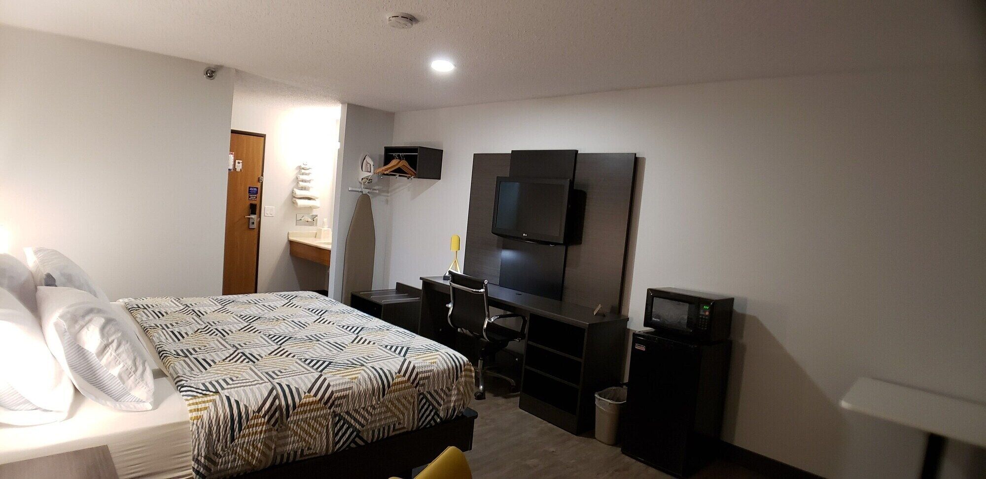 Una habitación de hotel con cama, escritorio, silla, televisor y microondas.