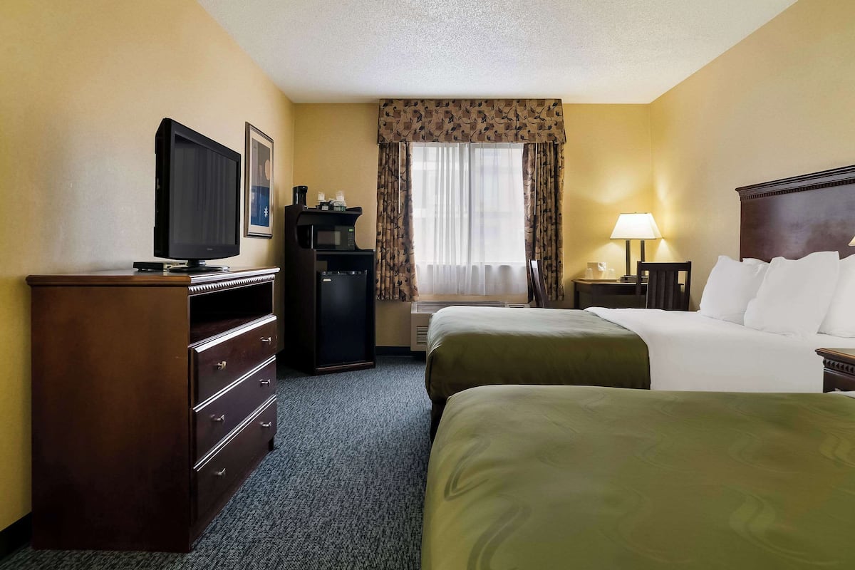 A hotel room with two beds, a TV, a desk, a lamp, and a minibar.