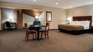 Una habitación de hotel con cama, escritorio con silla, mesa con dos sillas, lámpara y espejo.