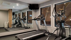 Un gimnasio con cintas de correr, elípticas y un espejo grande.