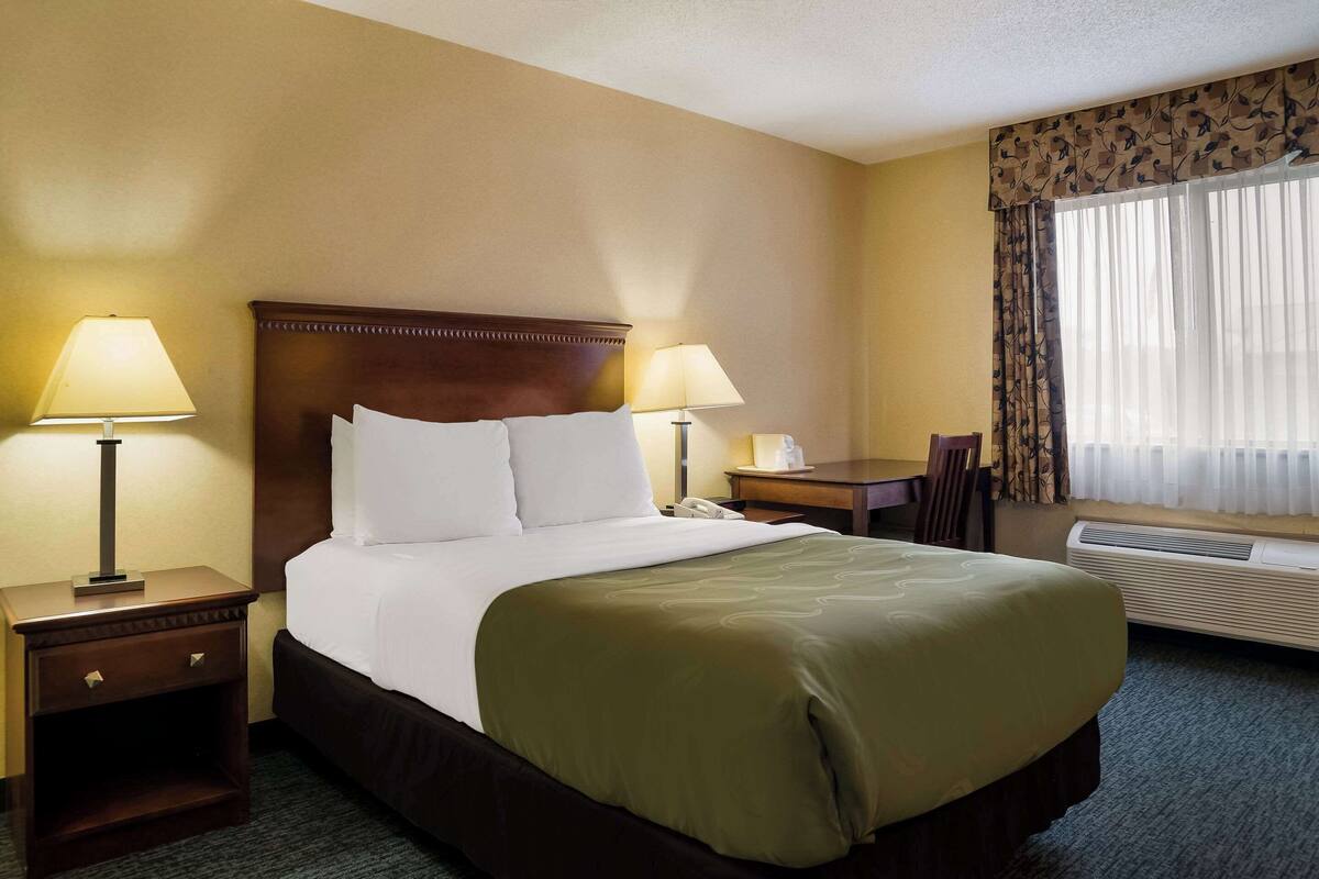 A hotel room with a large bed, two bedside tables with lamps, a desk, and a chair.