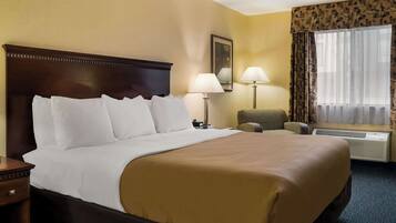 A hotel room with a large bed, two bedside lamps, a chair, a window with curtains, and an air conditioning unit.