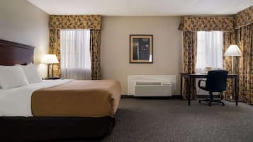 A hotel room with a bed, a desk, a chair, a lamp, and a picture on the wall.