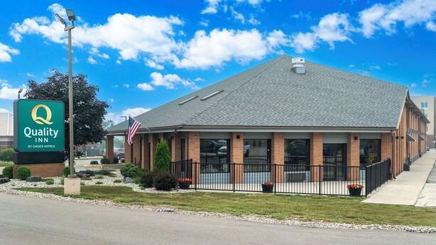 A Quality Inn by Choice Hotels building with a brick facade, a black metal fence, and an American flag.