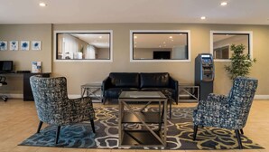 Un hall de hotel con un sofá de cuero negro, dos sillones estampados, una mesita y un mostrador de recepción con una computadora y una caja registradora.