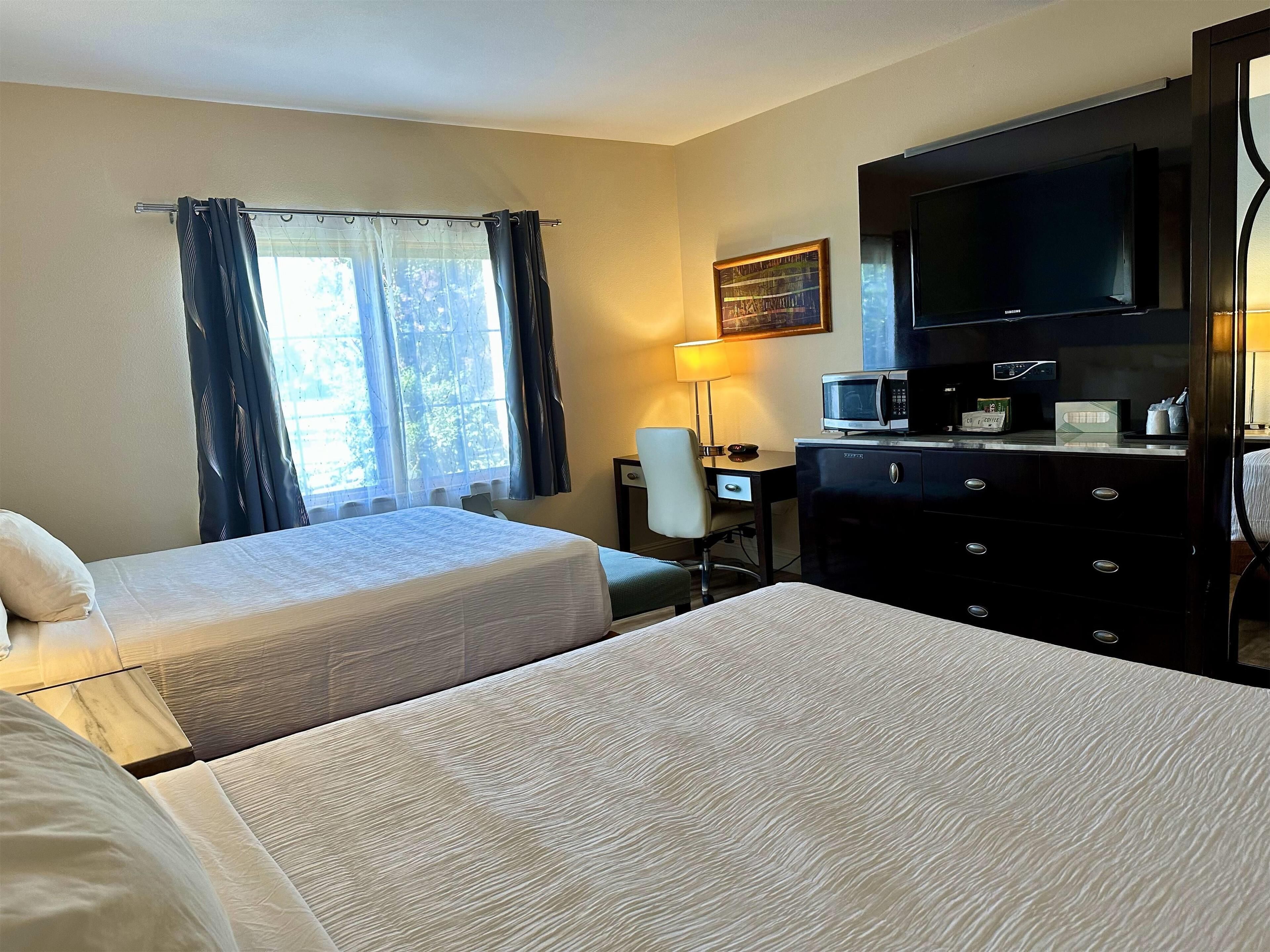 A hotel room with two beds, a desk with a chair, a television, a lamp, and a dresser.