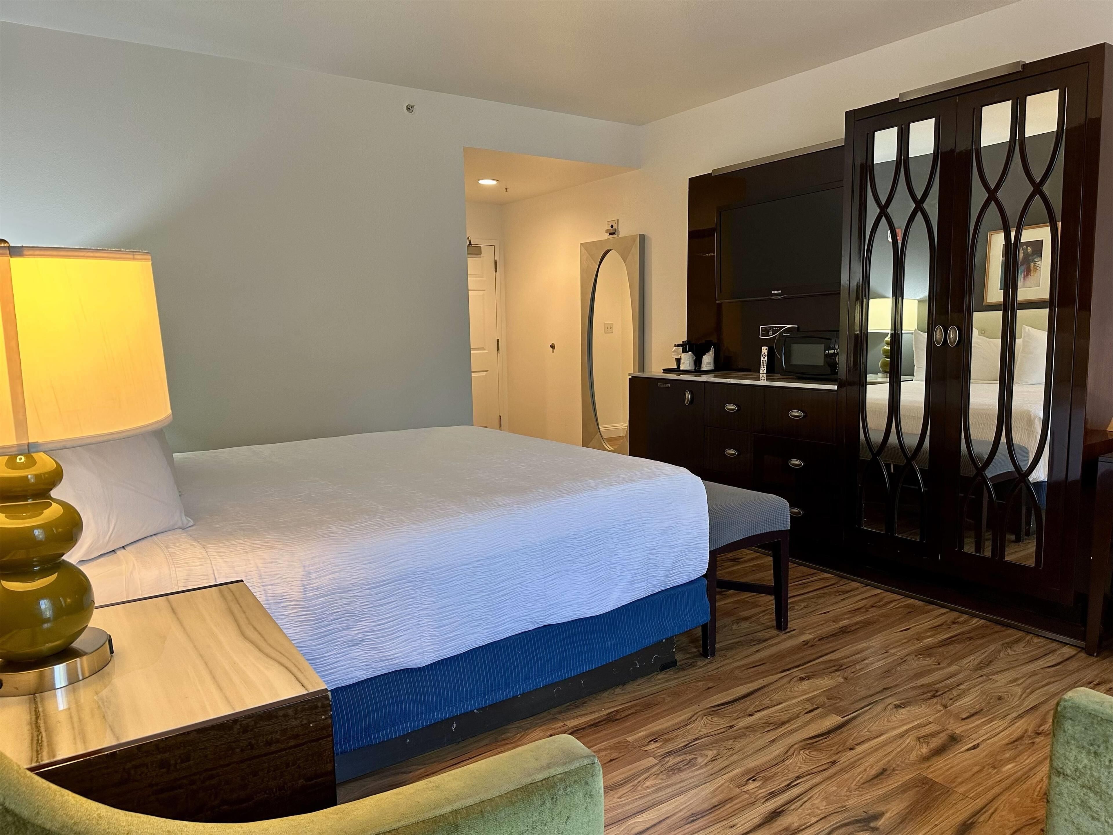 Una habitación de hotel con una cama, un escritorio, una lámpara, un aparador y un armario.