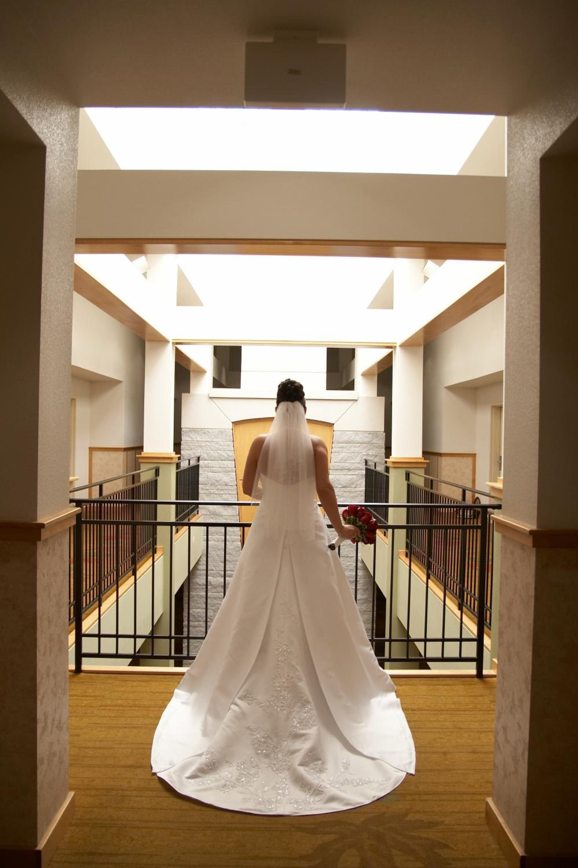 Una sposa con un abito da sposa bianco scende una scala in un atrio di un hotel, con vista sul cielo attraverso un lucernario.
