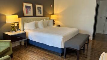A neatly arranged hotel room with a large bed, bedside lamps, a digital clock, and a bench.