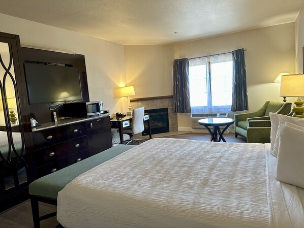 A hotel room with a large bed, a desk with a chair, a television, a fireplace, and a window with curtains. - Rocklin Park Hotel, Trademark Collection by Wyndham (Rocklin)