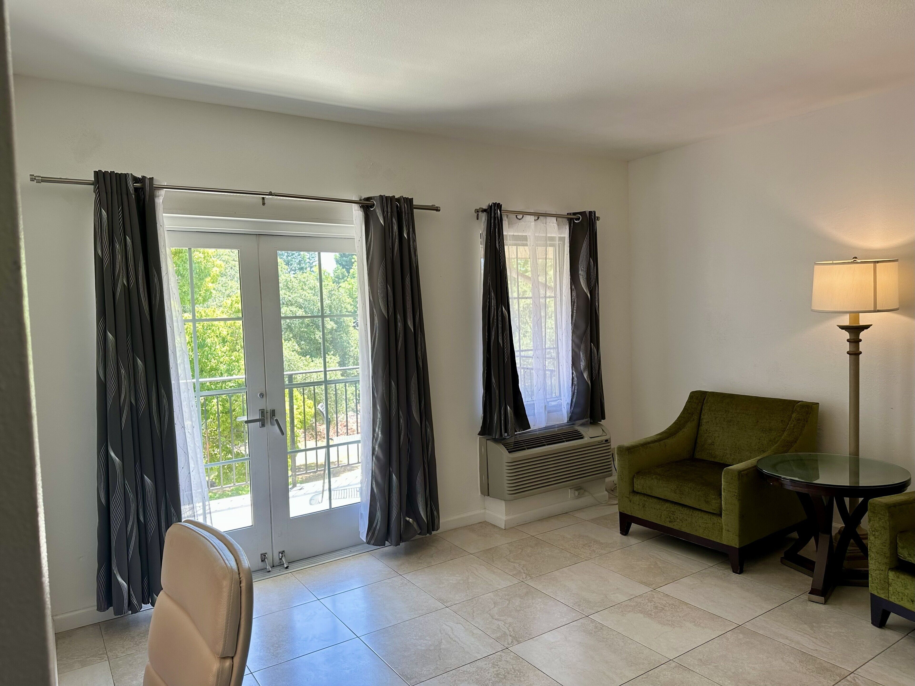 A room with a sliding glass door, a green armchair, a small round table, a floor lamp, and a wall-mounted air conditioning unit.