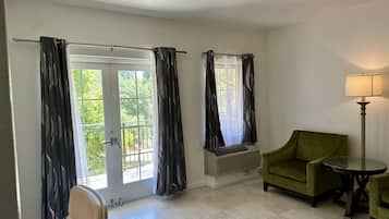 A room with a sliding glass door, a green armchair, a small round table, a floor lamp, and a wall-mounted air conditioning unit.