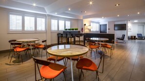 A spacious room with multiple seating arrangements, including round tables and chairs, a television, and a fire extinguisher. - The Crestview (Mountain View)
