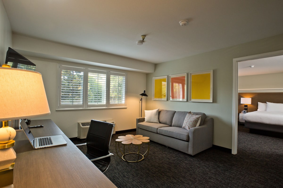 A hotel room with a desk, laptop, chair, sofa, and a bed.