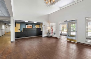 A reception area with a dark reception desk, a welcome sign, a flag, and a chandelier. - Extended Stay America Suites Dallas Plano Parkway (Plano)