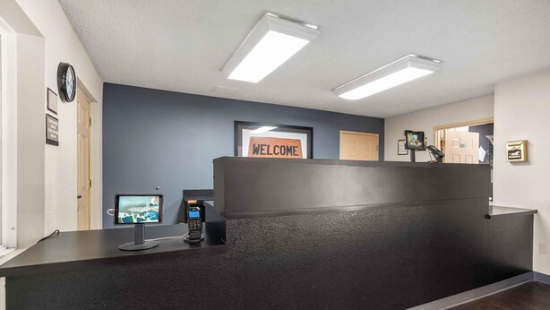 A reception desk with a 'WELCOME' sign, a digital screen, a phone, and a clock on the wall. - Extended Stay America Suites Dallas Plano Parkway (Plano)