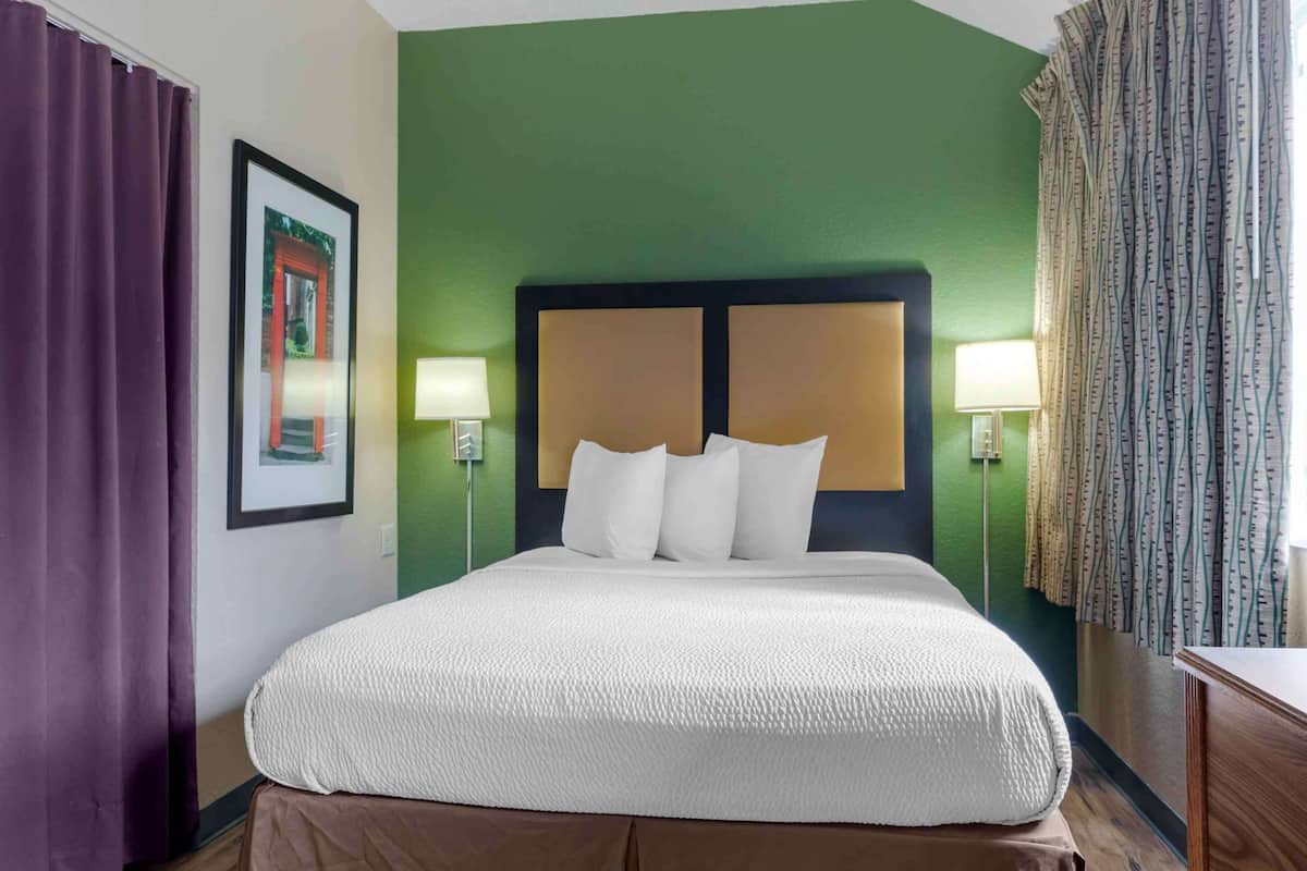 A hotel room with a large bed, green walls, and purple curtains.
