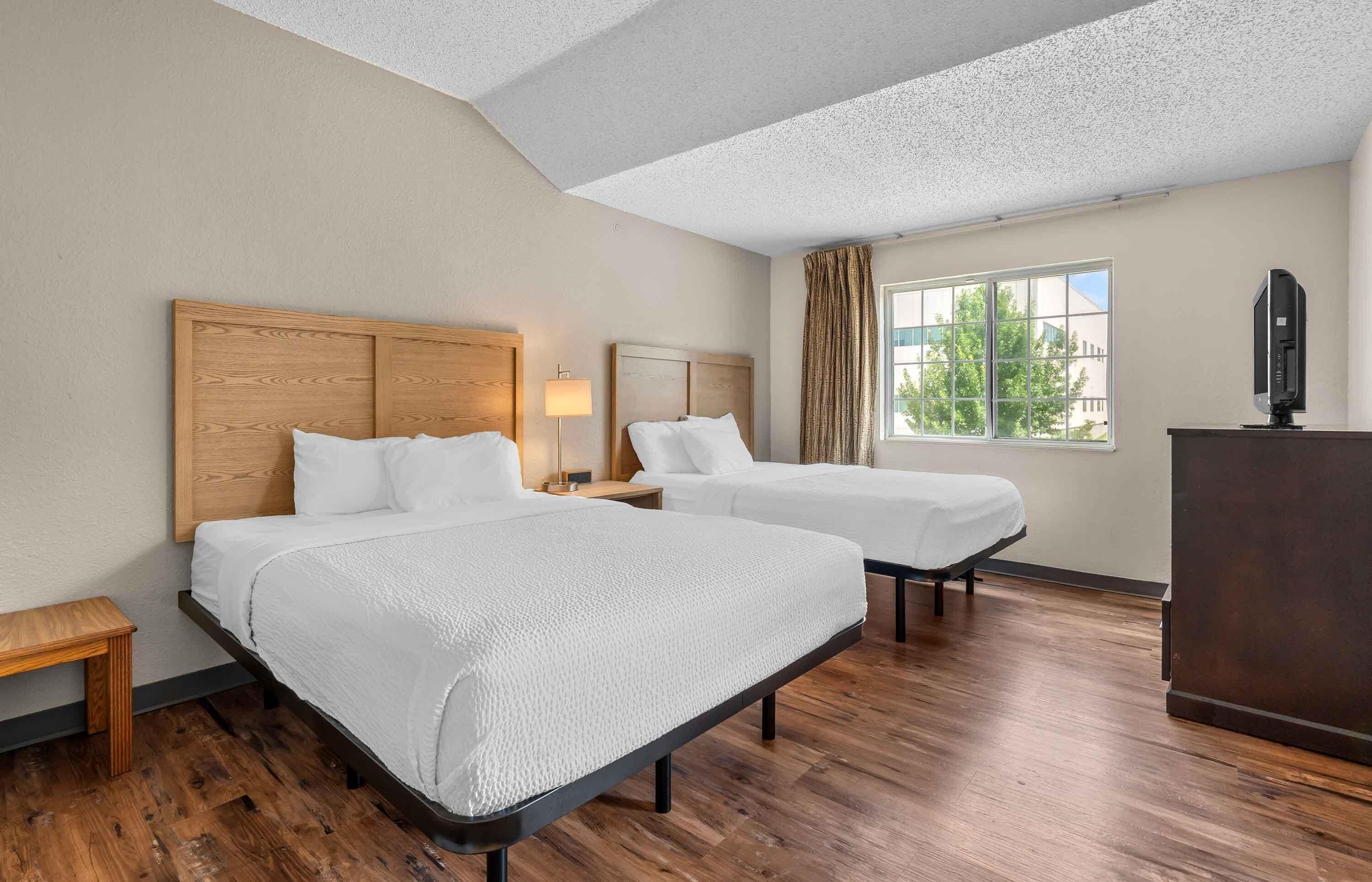 A hotel room with two beds, a desk, a television, and a window with curtains.