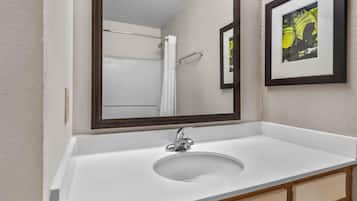 A bathroom with a white sink, a mirror, and a framed picture on the wall.