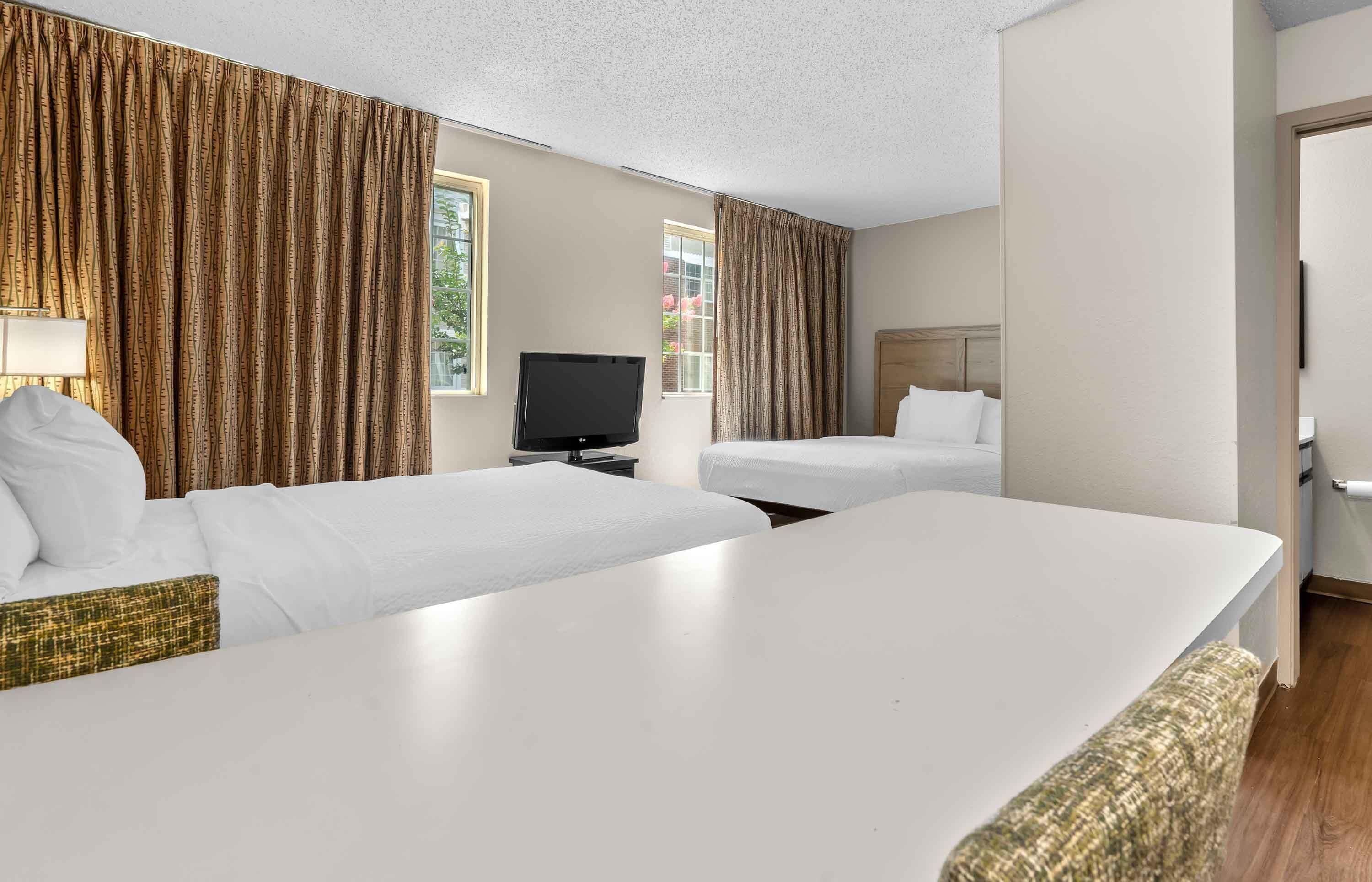 A hotel room with two beds, a TV, and a window with curtains.