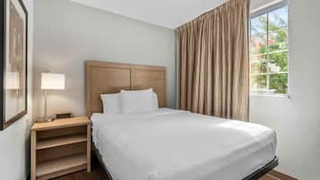 A hotel room with a bed, a nightstand, a lamp, and a window with curtains.