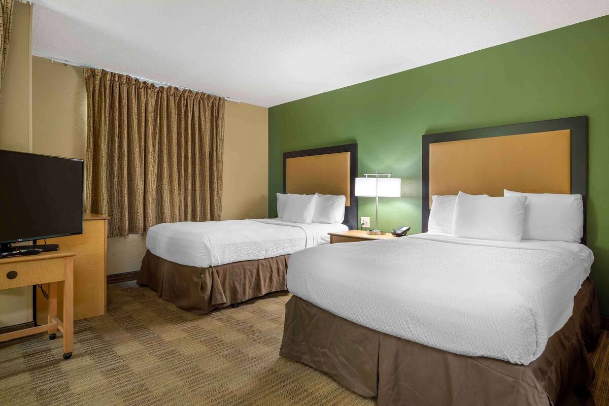 A hotel room with two beds, a television, a desk, and a lamp.