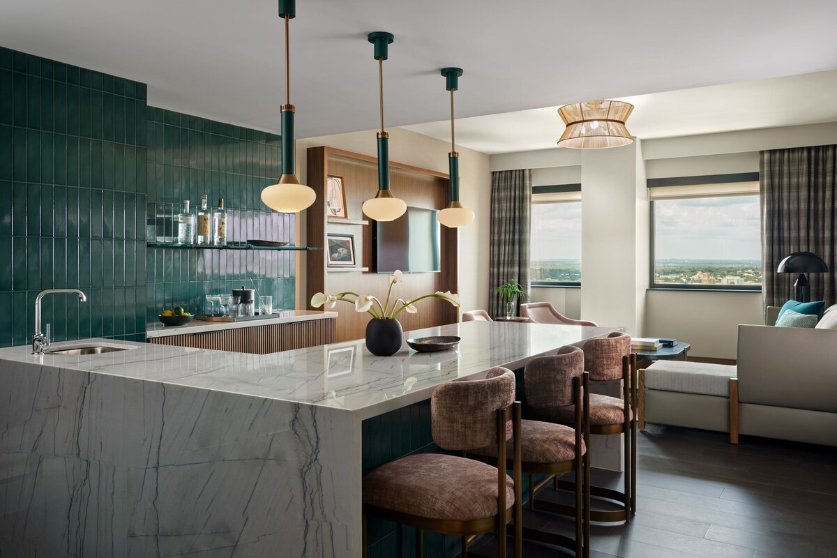 Una cocina moderna con una isla de mármol, luces colgantes y vistas a la ciudad.