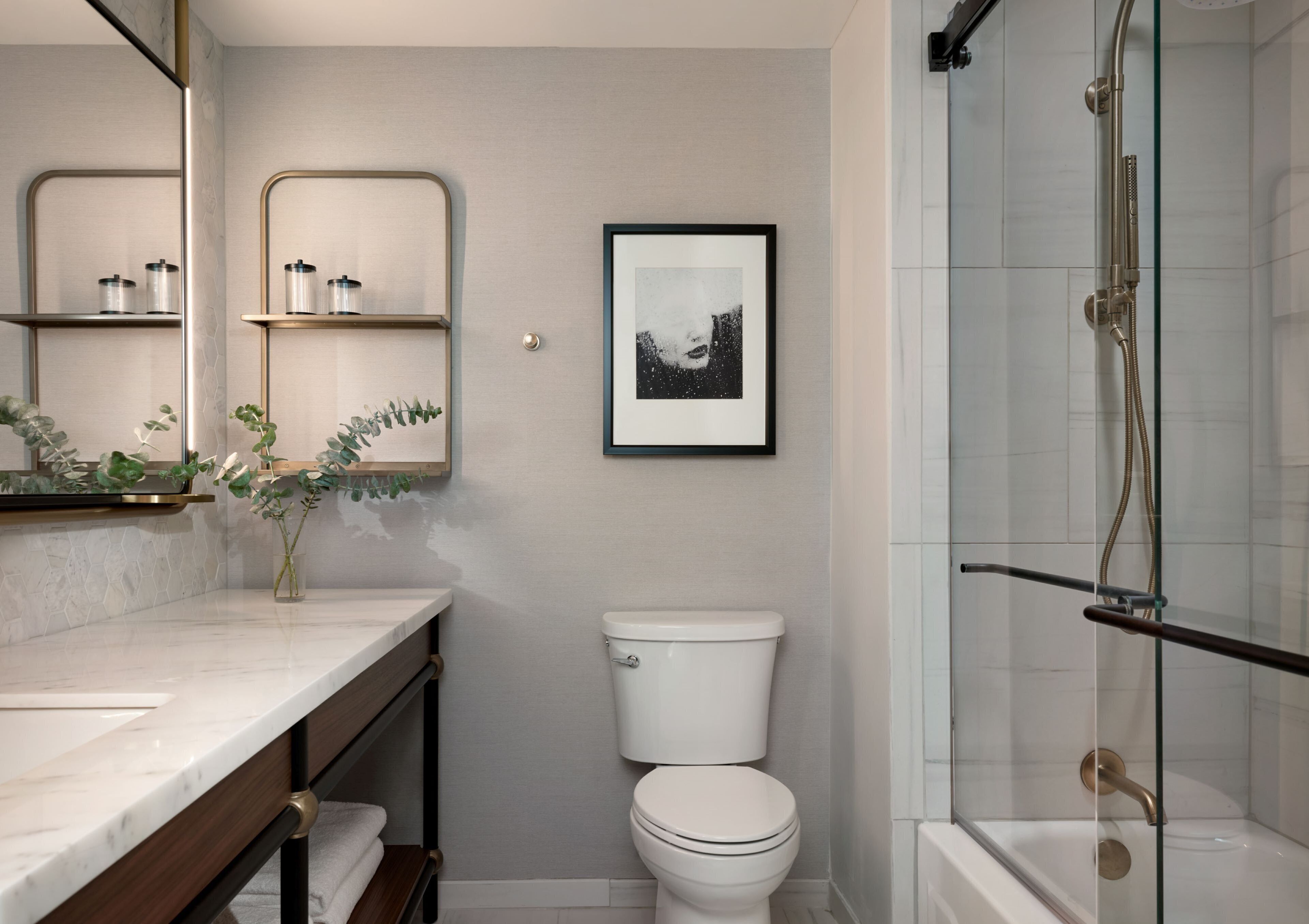 A bathroom with a white toilet, a glass shower enclosure, a marble countertop, and a framed picture on the wall.