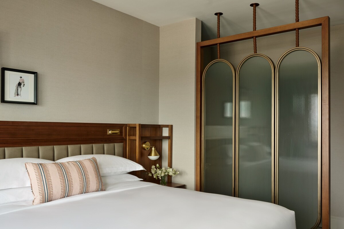 Habitación de hotel con una cama grande, cabecera de madera, un cuadro enmarcado en la pared y una puerta corrediza de vidrio con paneles esmerilados.