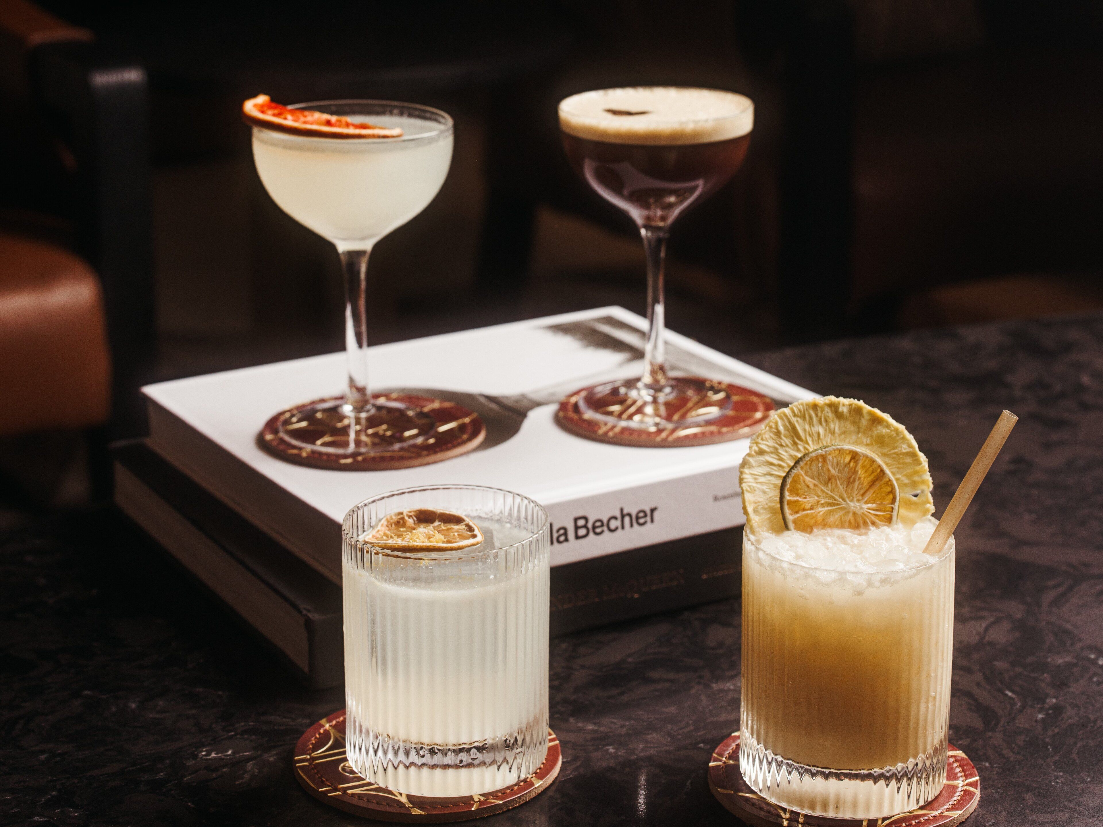 Three cocktails on a table with a book titled "La Becher" in the background.