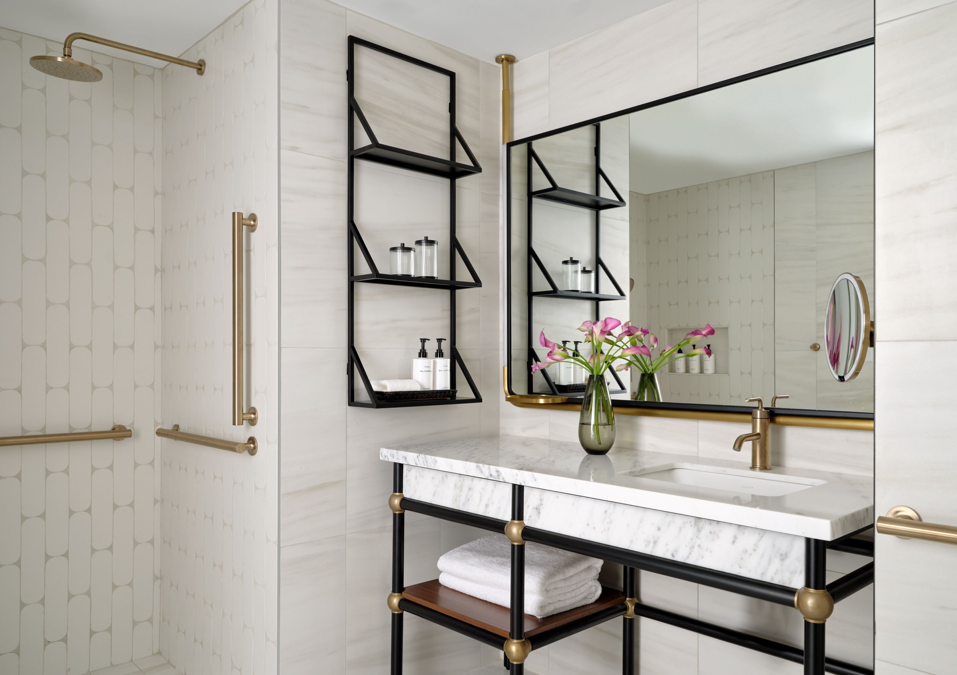 A modern bathroom with a marble vanity, black metal shelving, a large mirror, and a shower with gold fixtures.