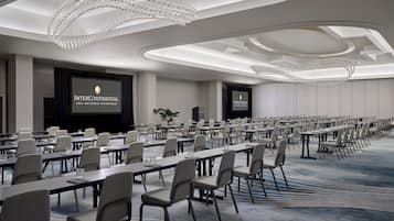A conference room with rows of tables and chairs, a large screen, and a chandelier.