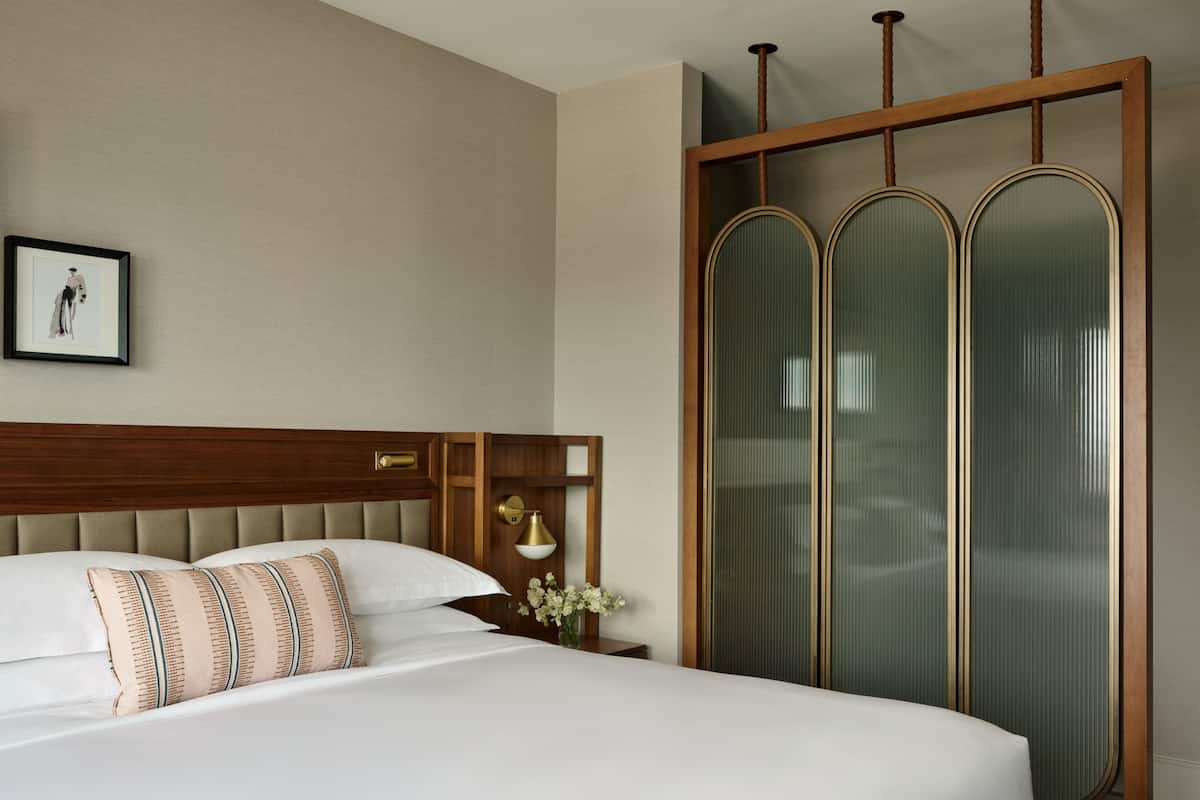 Habitación de hotel con una cama grande, cabecera de madera, un cuadro enmarcado en la pared y una puerta corrediza de vidrio con paneles esmerilados.